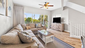 A modern living room with a sectional sofa, a glass coffee table, and a ceiling fan.