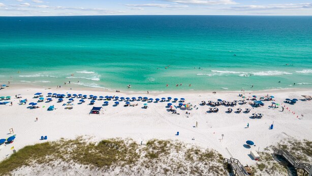 A beach with white sand, clear turquoise water, and numerous umbrellas.