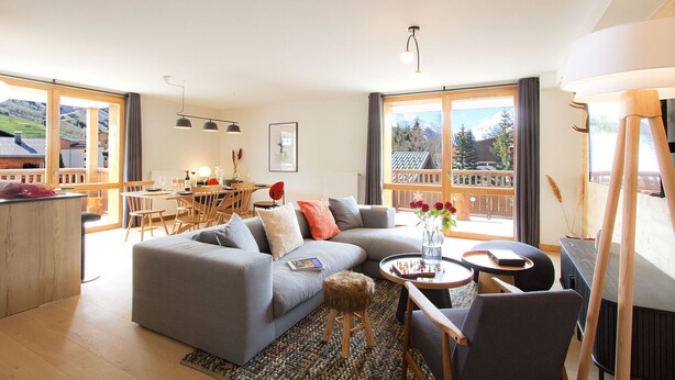 Una sala de estar moderna con un sofá gris, una mesa de centro y un comedor con mobiliario de madera.