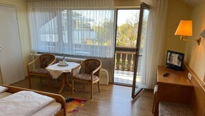 Et hotelværelse med seng, et lille bord med stole, et fjernsyn og en balkon med udsigt.