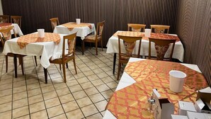 En restaurant med flere borde og stole, alle dækket med dug. Væggene har en panelering, og der er lys i loftet.
