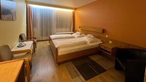 Et hotelværelse med en dobbeltseng, et skrivebord, en stol, et lille bord og en radiator.