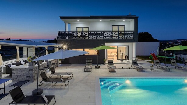 Una moderna casa a due piani con un balcone, un'area salotto esterna e una piscina.