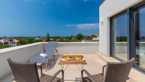 A balcony with a table set for breakfast, two wicker chairs, and a view of the sea and buildings. - Beautiful home in Porec (Porec)