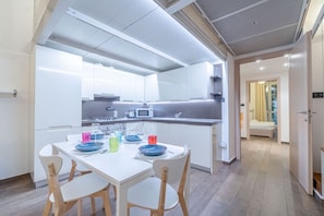 A modern kitchen with white cabinetry, a dining table with chairs, and a visible microwave.