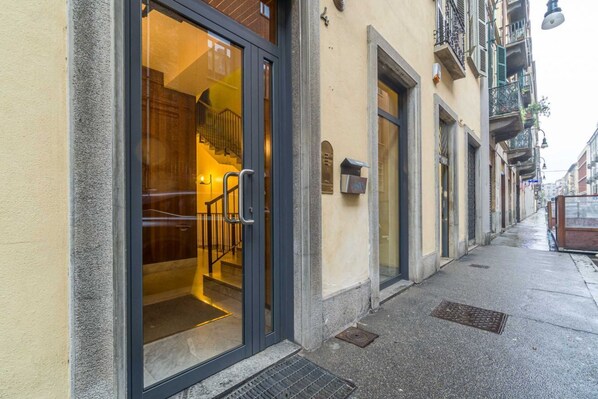 A hotel entrance with a glass door, a visible staircase inside, and a narrow sidewalk.