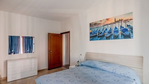Un dormitorio con cama, cómoda, una puerta y un cuadro de barcos en la pared.