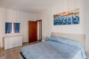 A bedroom with a bed, a dresser, a door, and a wall painting of boats.