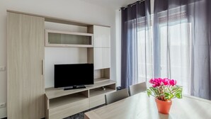 Una habitación moderna con un televisor sobre un soporte de madera, una mesa de comedor y una planta en maceta.