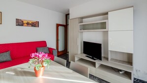 Una sala de estar moderna con un sofá rojo, un televisor sobre un mueble de madera y una planta en maceta sobre la mesa.