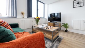 A modern living room with a sofa, coffee table, and a flat-screen TV. - Chic Industrial Luxury Stay (Stretford)