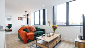 A modern living room with a green sofa, a wooden coffee table, and large windows offering a city view. - Chic Industrial Luxury Stay (Stretford)