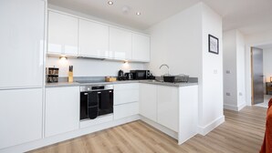 A modern kitchen with white cabinetry, a built-in oven, and a microwave. - Chic Industrial Luxury Stay (Stretford)