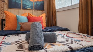 Una cama bien hecha con almohadas coloridas, una colcha estampada y toallas enrolladas.