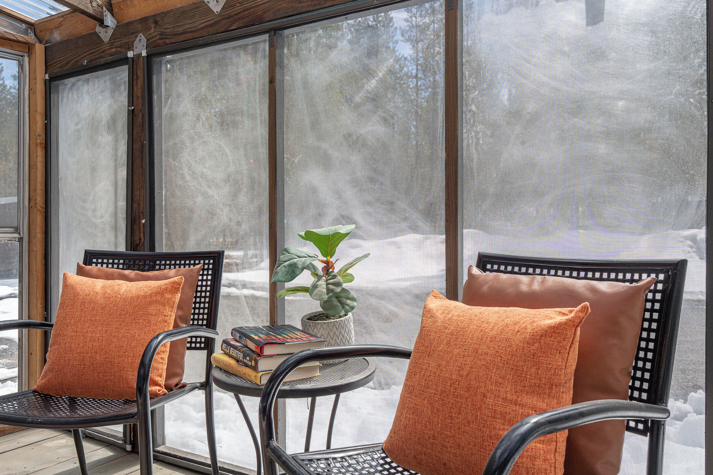A cozy seating area with two chairs, each with an orange cushion, and a small table with a plant and books.