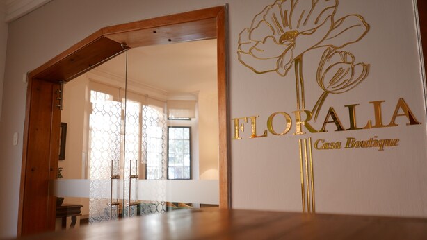 Ein Zimmer mit Holzboden, einer Glastür, die in einen anderen Raum führt, und einer Wand mit floralem Dekor und dem Schriftzug "FLORALIA Casa Boutique".