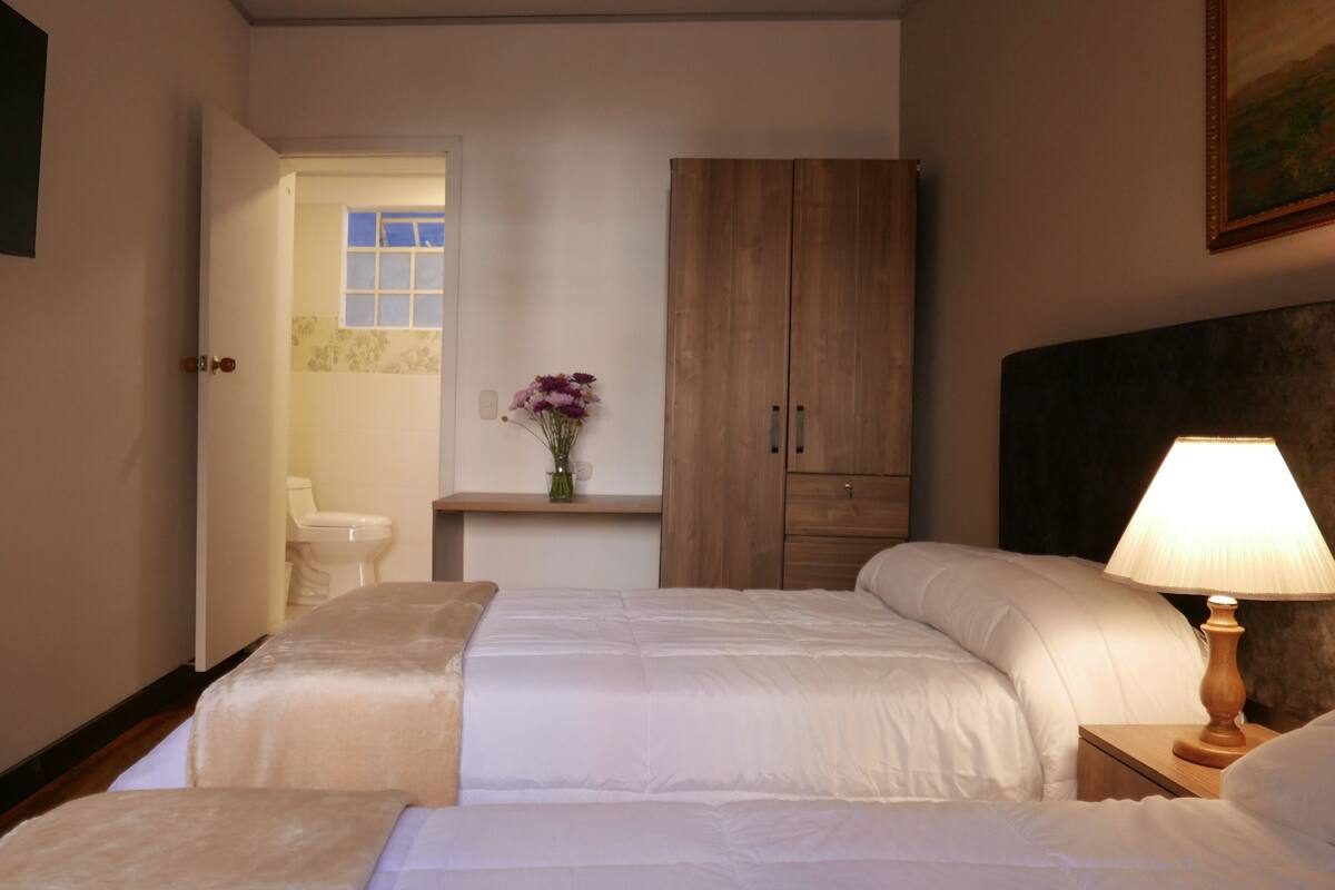 Ein Hotelzimmer mit zwei Betten, einem Holzschrank, einem Nachttisch mit Lampe sowie einem kleinen Tisch mit Blumenvase.