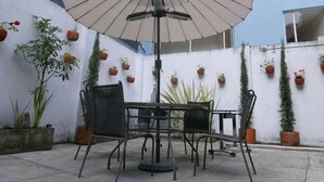 Eine Terrasse mit Tisch und Stühlen, einem Sonnenschirm und Kübelpflanzen an einer Wand.