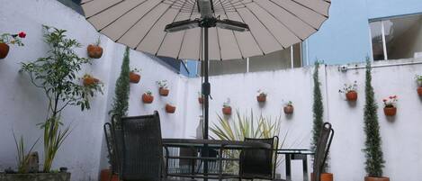 Un espace patio aménagé avec une table et des chaises, un parasol et des plantes en pot disposées contre un mur.