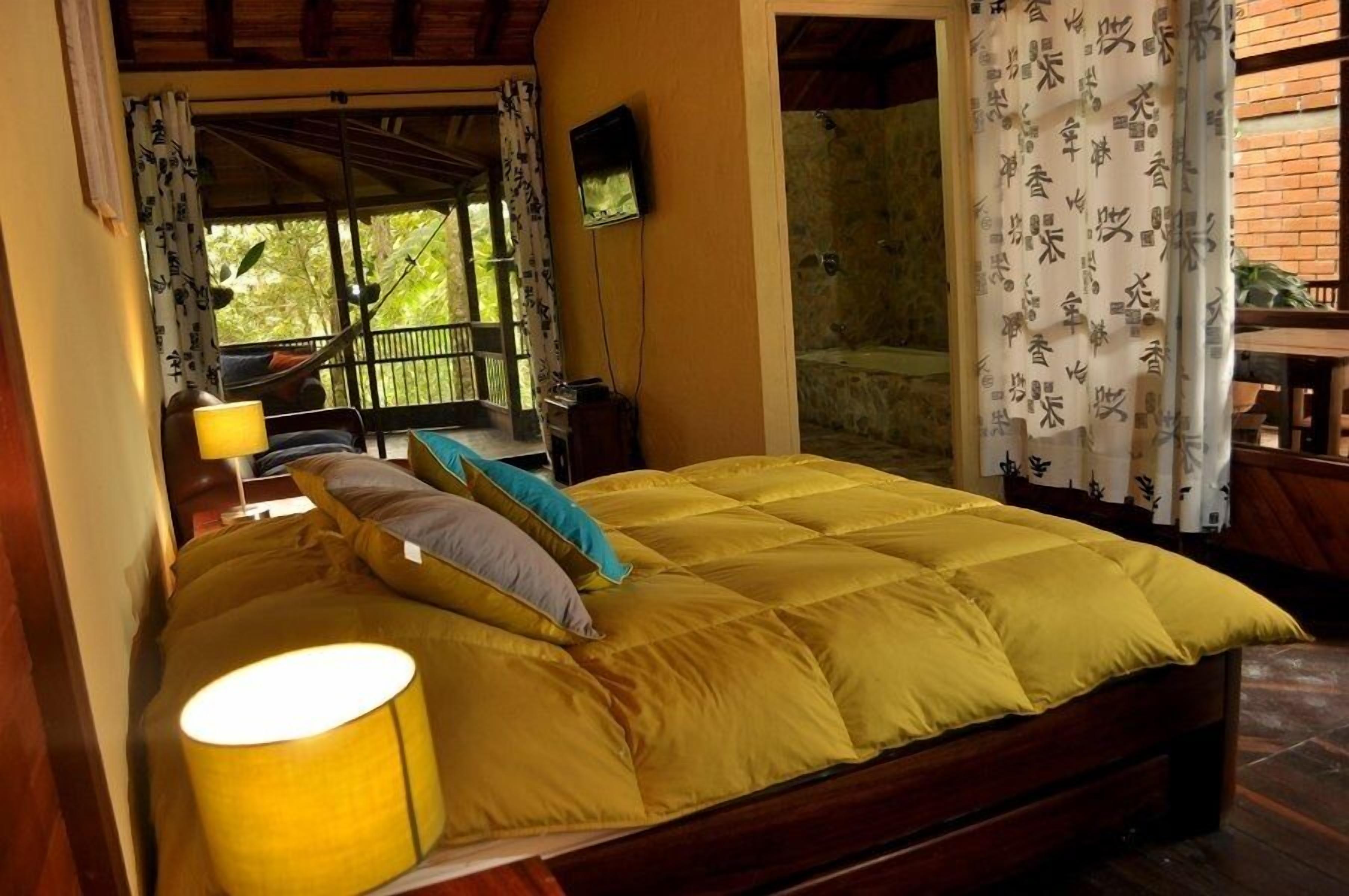 A room with a bed, a TV, and a view of a balcony with a railing.