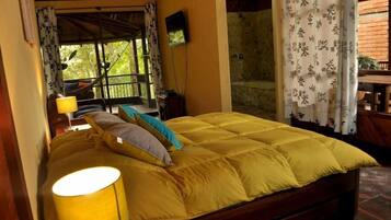 A room with a bed, a TV, and a view of a balcony with a railing.