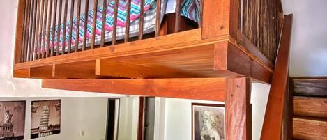 A room with a wooden bunk bed, a bed with a colorful zigzag bedspread, and a small seating area with cushions.