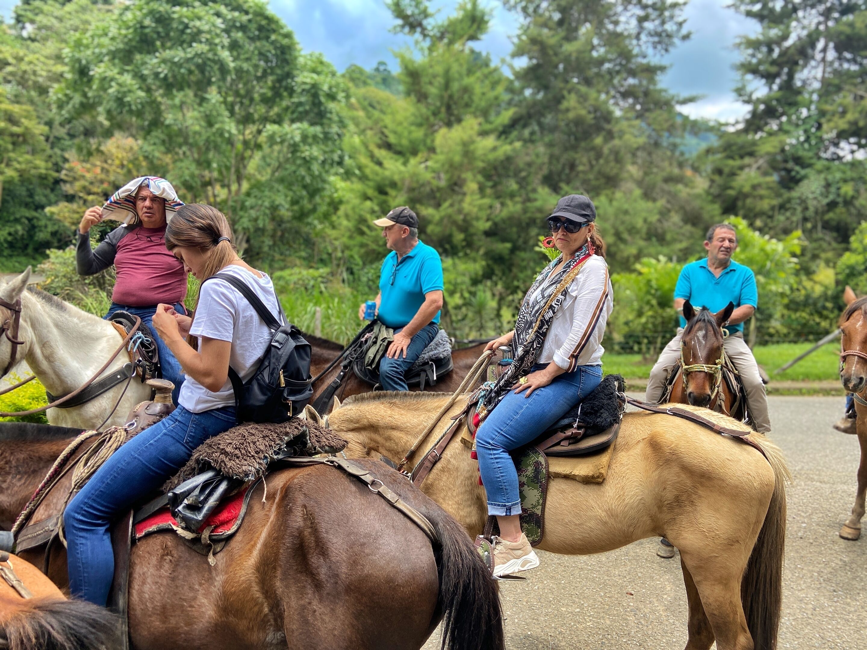 A group of people riding horses on a dirt path surrounded by greenery.