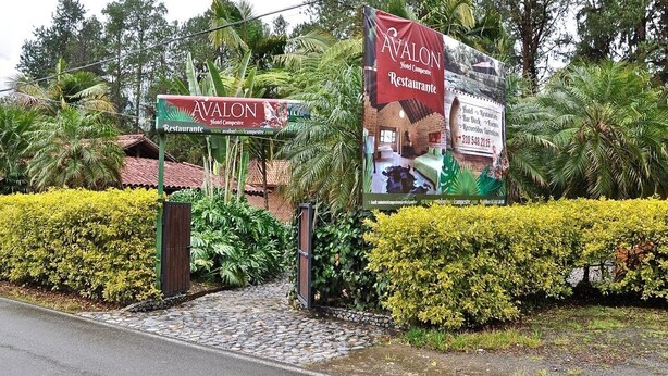 Entrada de hotel con un cartel que dice 'Avalon Hotel & Restaurant' y un gran banner promocional.