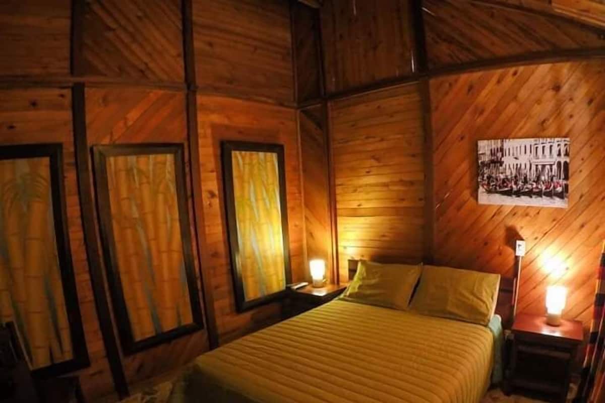 A wooden cabin bedroom with a bed, two bedside tables with lamps, and a framed picture on the wall.