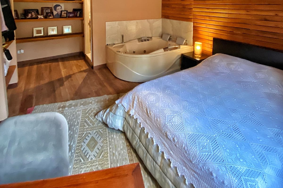 A bedroom with a large bed, a bathtub, and a wooden ceiling.