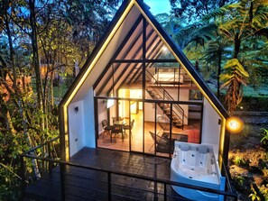Una cabaña moderna de forma triangular con fachada de vidrio, un jacuzzi y una escalera que lleva a un dormitorio en el altillo.