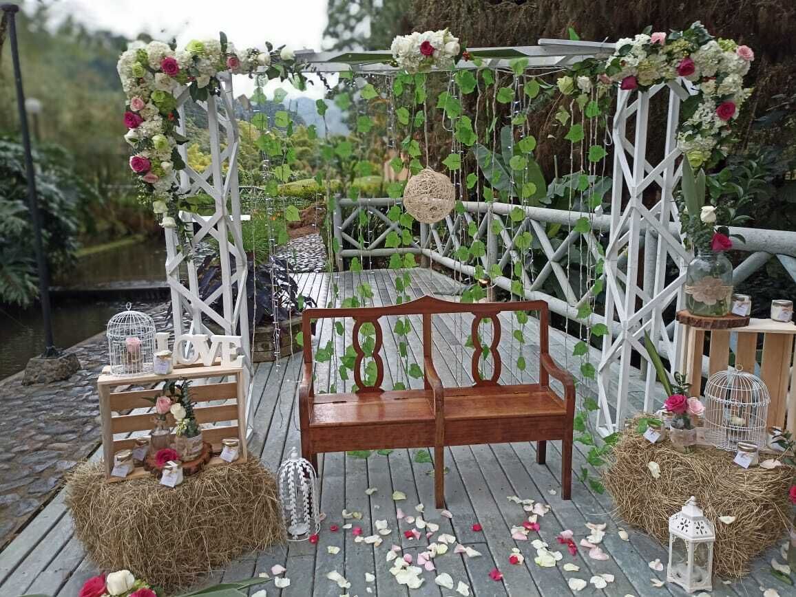 Un banco de madera bajo un arco de celosía blanca adornado con flores y adornos colgantes.
