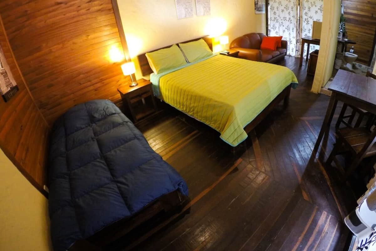A room with two beds, wooden flooring, and a dining area.