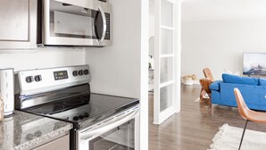 Une cuisine moderne dotée d’appareils électroménagers en acier inoxydable, un coin repas avec un canapé bleu et une table d’appoint en bois, et une porte blanche donnant sur une autre pièce.