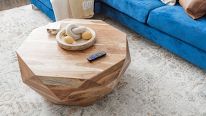 Une table basse hexagonale en bois, sur laquelle se trouvent un bol d’œufs et une télécommande.