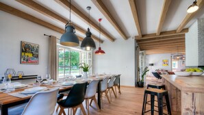 A dining area with a long wooden table, multiple chairs, hanging pendant lights, and a view of the outdoors through large windows. - Awesome home in Porec (Porec)