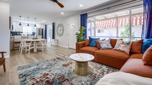 Ein modernes Wohnzimmer mit einem braunen Sofa, einem runden Couchtisch und einem großen Fenster mit Vorhängen.