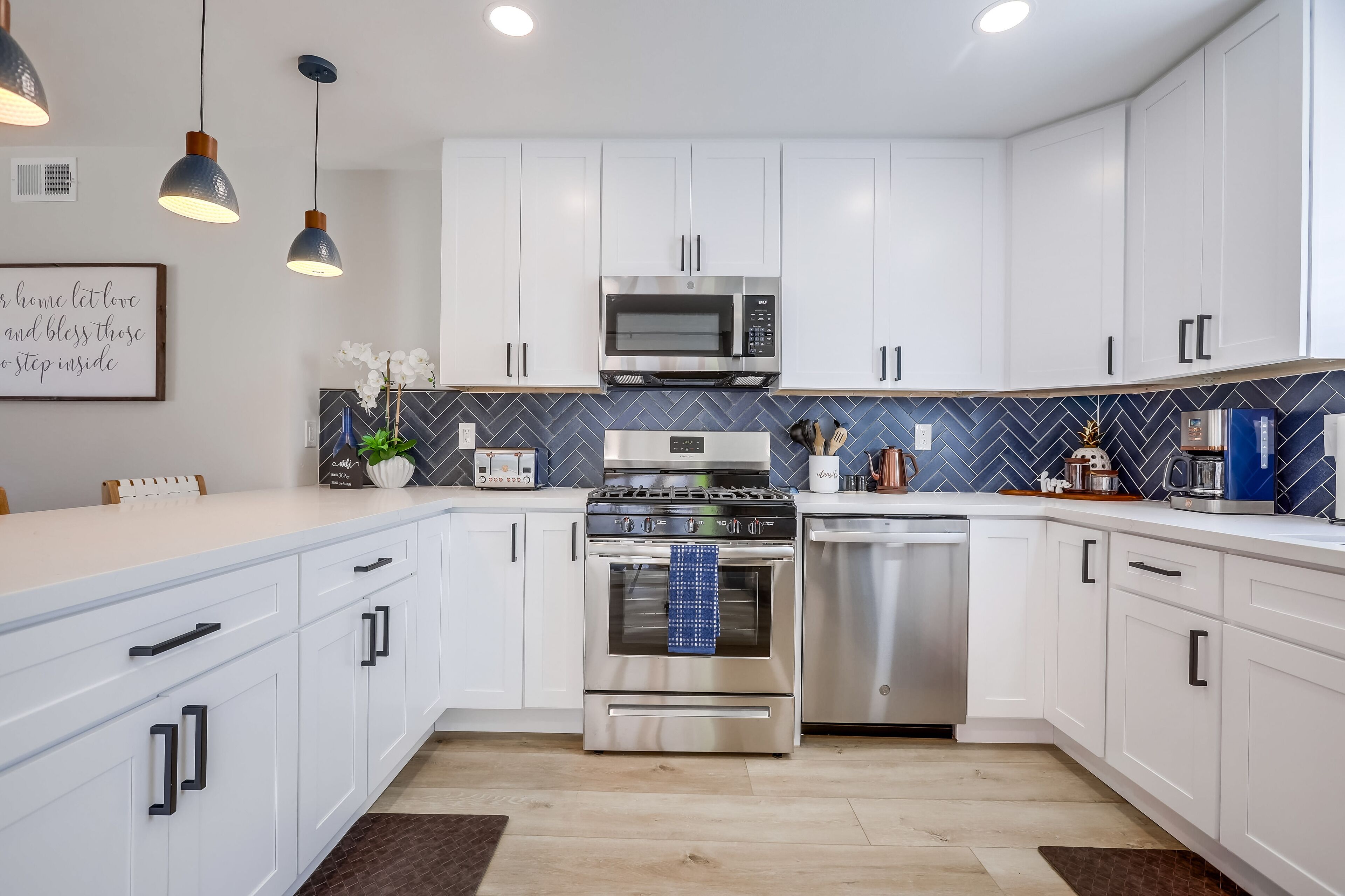 A modern kitchen with white cabinets, stainless steel appliances, and a blue herringbone backsplash.