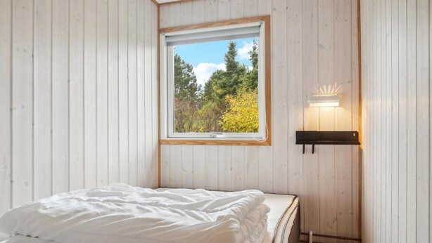 A bedroom with a bed, a window with a view of trees, and a wall-mounted light fixture. - Nice home in Bogø By with WiFi (Bogø By)