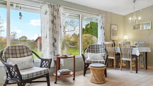 A cozy room with a large window, wicker chairs, a round table, and a dining table. - Nice home in Bogø By with WiFi (Bogø By)