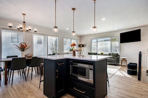 A modern kitchen with a central island, black cabinetry, stainless steel appliances, and pendant lighting.