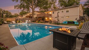 A backyard with a swimming pool, a fire pit, outdoor furniture, and a wooden deck.