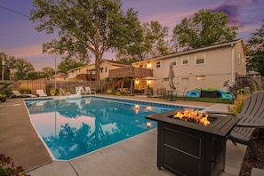 A backyard with a swimming pool, a fire pit, outdoor furniture, and a wooden deck.