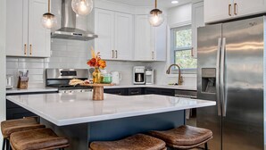 A modern kitchen with white cabinetry, stainless steel appliances, and a central island with bar stools.