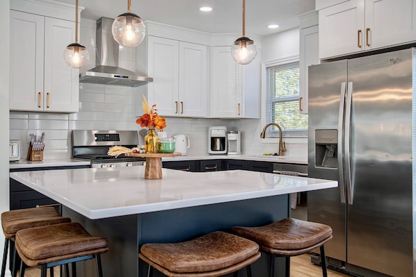 A modern kitchen with white cabinetry, stainless steel appliances, and a central island with bar stools.