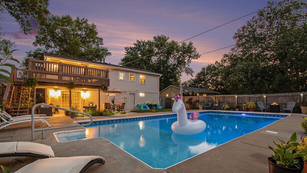 A backyard with a swimming pool, a white horse float, lounge chairs, and a house with a balcony.