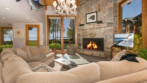 A cozy living room with a stone fireplace, comfortable seating, and a television. - Fleur Du Lac 16 By Tahoe Getaways - Lakefront Monthly Rental with Pool, Tennis, Gym, Boat Slip (Homewood)
