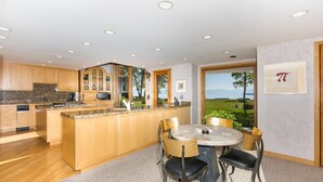 A modern kitchen with wooden cabinets, granite countertops, and a large island. There is a dining area with a round table and chairs, and a view of the outdoors through large windows. - Fleur Du Lac 16 By Tahoe Getaways - Lakefront Monthly Rental with Pool, Tennis, Gym, Boat Slip (Homewood)
