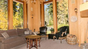 A spacious living room with a high ceiling, large windows, a chandelier, a sofa, a chair, a small table, and a stone fireplace. - Fleur Du Lac 16 By Tahoe Getaways - Lakefront Monthly Rental with Pool, Tennis, Gym, Boat Slip (Homewood)