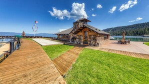 A stone building with a wooden deck, a dock, and a view of a lake. - Fleur Du Lac 16 By Tahoe Getaways - Lakefront Monthly Rental with Pool, Tennis, Gym, Boat Slip (Homewood)